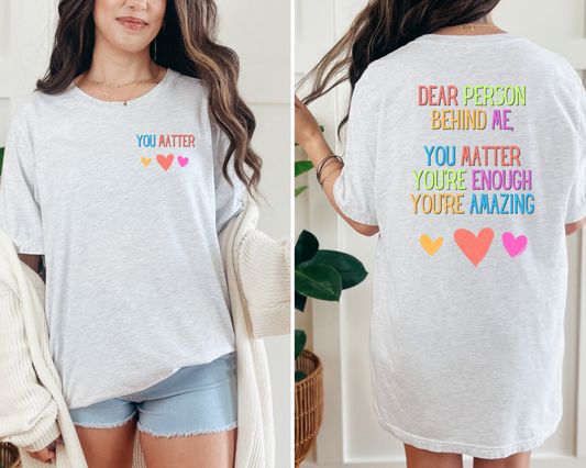 Person wearing a white t-shirt with motivational text and colorful hearts.